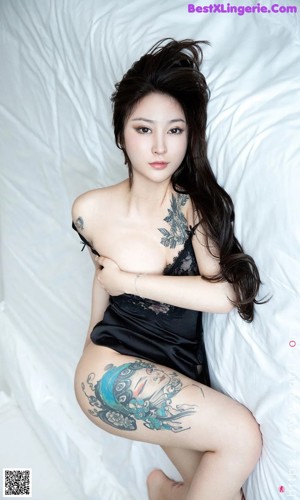 A woman laying on a bed with a tattoo on her arm.