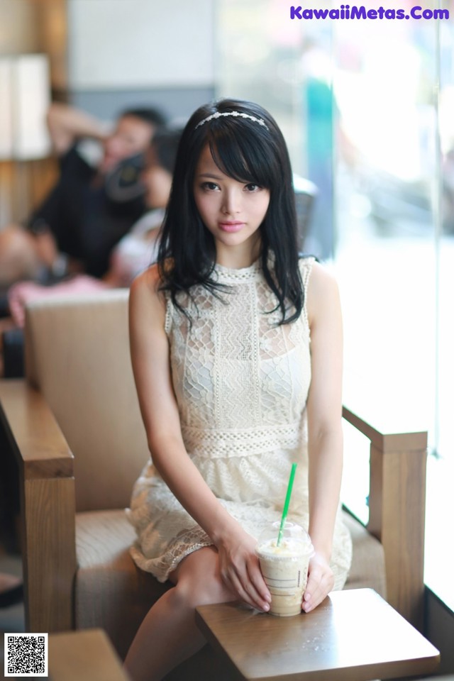 A woman sitting on a bench holding a drink.